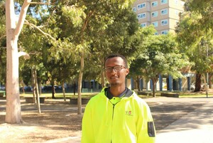 a man in a hi-vis jacket in front of the camera with a large open park behind him